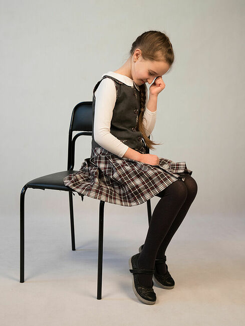 schoolgirl sits and cries on a light background